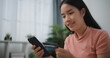 © Johnstocker - Portrait of Young asian woman sitting on sofa in living room, makes online banking payments through the internet from bank card on smartphone ,Shopping online with credit card.