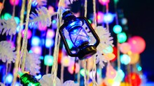 Close-up Of A Wired Electric Garland In The Form Of A Lantern And Many Others Blurred Behind It Glowing With Colorful Lights