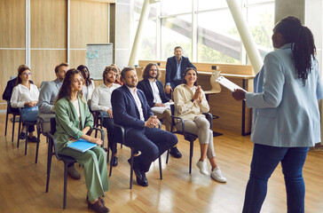 Wall Mural - Group of diverse business people on meeting discussing work project sitting in a row in office. Company employees listening their african americam woman colleague with a report in conference room. 