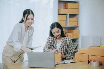 Wall Mural - Two beautiful Asian women are happy and excited after receiving a new order from an SME customer. Commercial inspection. online marketing Boxes for entrepreneurs, SME sellers and independent online sa