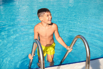 Boy leaving pool, looking up, sunlight on water. Depicts summer fun as an escape from the indoor, screen-heavy lifestyle