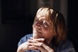 © Maskot - Smiling blond senior woman with hands on chin relaxing in sunlight at home