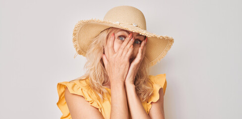 Portrait of woman covering eyes with hand, peeking through fingers isolated on white studio background