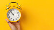 person holding alarm clock, Hand holding alarm clock isolated on yellow background