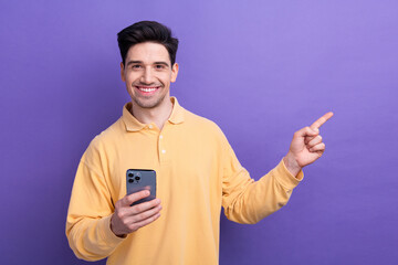 Wall Mural - Photo of positive cheerful guy wear yellow polo typing modern gadget pointing empty space isolated violet color background