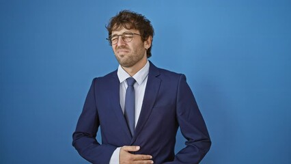 Canvas Print - Young man in business suit grapples with painful stomach ache, portraying anguish of illness against an isolated blue background