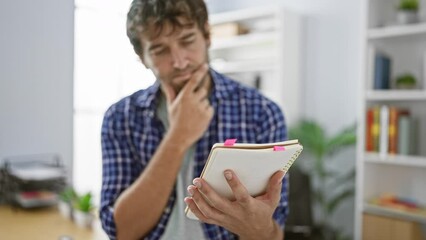 Poster - Worried, focused young man working hard at his job in the office, reading paperwork and thinking over his notebook, blond beard adding to his professional portrait