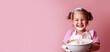 © IndigoElf - Сute little girl smile and make baked goods in a pink minimalist kitchen. Child soiled in flour, learning to cook, fun home activity, copy space for text.