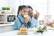 African little child girl eating homemade sandwiches in hands, standing in kitchen at home with brother, prepare food for breakfast. Siblings, kids make sandwich. Selective focus on girl