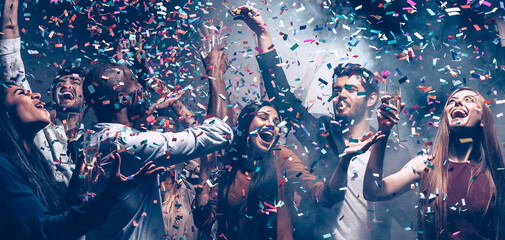 Poster - Group of happy young friends dancing and having fun in night club together while confetti flying around