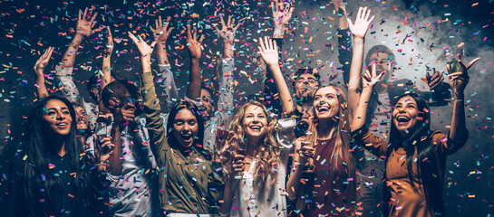 Wall Mural - Happy young people dancing and celebrating New Year in the night club while confetti flying around