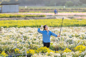 Canvas Print - Woman use digital camera with long stick pole to take photo over the flower farm