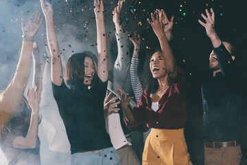 Wall Mural - Group of happy young people dancing and throwing confetti while having fun in night club together