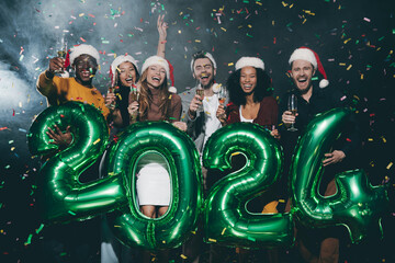 Wall Mural - Young friends holding flutes with champagne while celebrating 2024 New Year in night club together