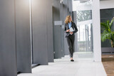 Fototapeta  - Confident businesswoman holding tablet walking in office