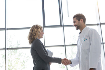 Wall Mural - Businesswoman and doctor shaking hands in hospital