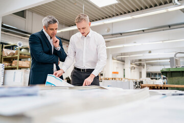 Two businessmen discussing paper in a factory