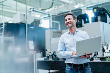 Happy mature businessman holding laptop while working in industry