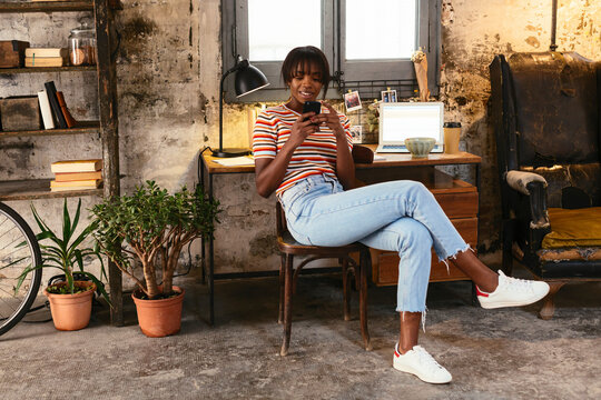 Young woman sitting in front of a desk in a loft using cell phone