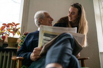 Wall Mural - Happy young woman and senior man with newspaper at home