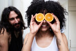 Happy young woman covering her eyes with oranges in kitchen