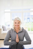 Fototapeta  - Smiling senior woman with hands clasped exercising at home
