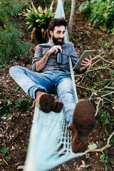 Wall Mural - Man lying in hammock drinking beer and using tablet