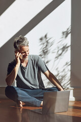 Wall Mural - Mature man on the phone sitting on the floor at home with laptop