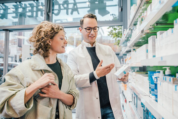 Pharmacist recommending medicine to smiling customer in chemist shop