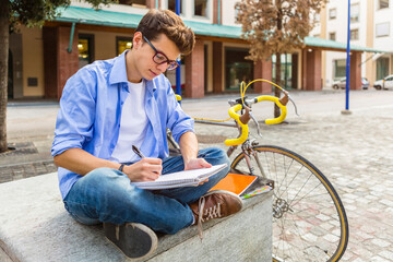 Wall Mural - Young man with racing cycle sitting on bench writing on notepad