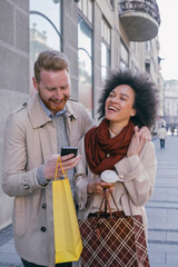 Wall Mural - Happy couple in the city with cell phone and shopping bags