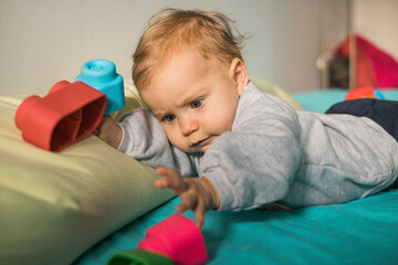 Portrait of baby girl lying on bed playing with plastic toy