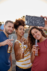 Wall Mural - Three friends with beer bottles taking selfie on the beach