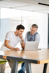 Senior businessman working with young colleague, using laptop