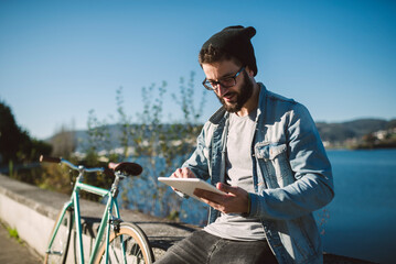 Wall Mural - Smiling young man using a tablet at the waterfront