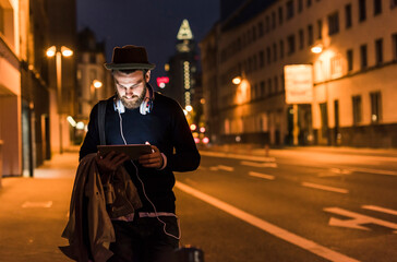 Wall Mural - Stylish young man with tablet on urban street at night