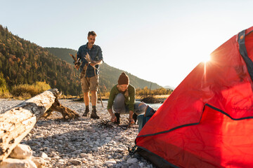 mature couple camping at riverside, collecting wood for a camp fire