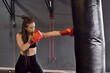 © tunedin - Female boxer wearing red gloves practicing boxing drill on punching bag in gym