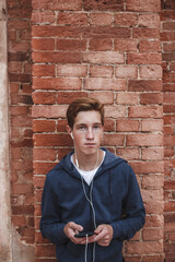 Wall Mural - Portrait of young man with cell phone and earphones at brick wall