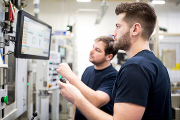 Canvas Print - Two men working in a modern factory operating a machine together