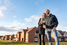 Happy Couple Looking Away While Standing Outside Newly Built Houses Against Sky