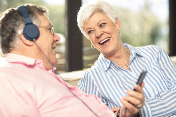 Wall Mural - Happy senior couple with cell phone and headphones on couch at home