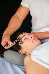 Wall Mural - Woman getting face massage with a facial cooling metal roller. Professional skin care treatment.