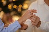 Fototapeta  - Making proposal. Man putting engagement ring on his girlfriend's finger against blurred lights, closeup