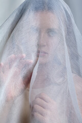 Wall Mural - Portrait of a young woman covered with white mesh fabric. A woman hides her face behind a veil cloth.