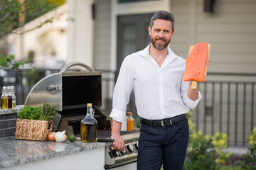 Poster - Man at a barbecue grill. Male cook preparing barbecue salmon fillet outdoors. Bbq salmon, grill for picnic. Roasted fish. Cook preparing barbeque in the house yard. Barbecue and grill.