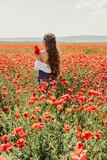 Fototapeta Kuchnia - Woman poppies field. Back view of a happy woman with long hair in a poppy field and enjoying the beauty of nature in a warm summer day.