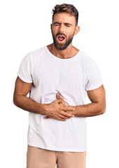 Young hispanic man wearing casual white tshirt with hand on stomach because nausea, painful disease feeling unwell. ache concept.