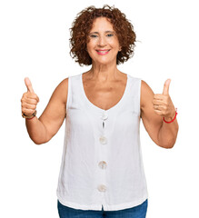 Wall Mural - Beautiful middle age mature woman wearing casual white shirt success sign doing positive gesture with hand, thumbs up smiling and happy. cheerful expression and winner gesture.