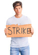 © Krakenimages.com - Young handsome man holding strike banner cardboard thinking attitude and sober expression looking self confident